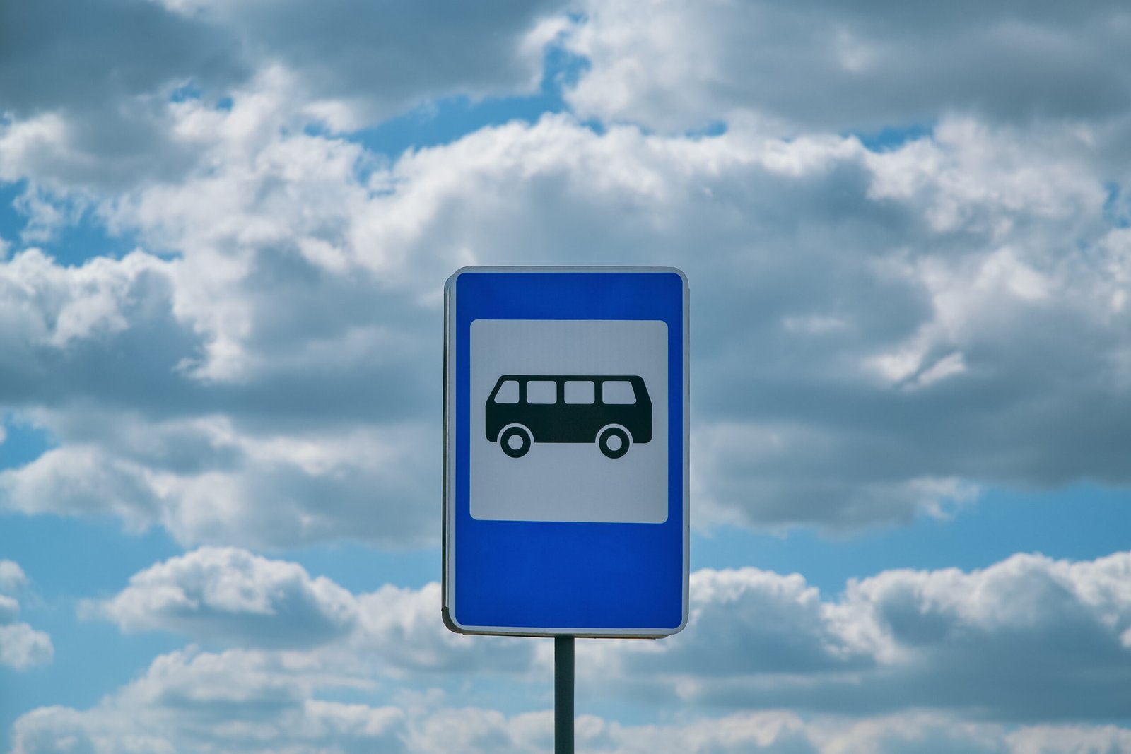 Blue and white bus stop sign depicting a bus against white clouds and a blue sky